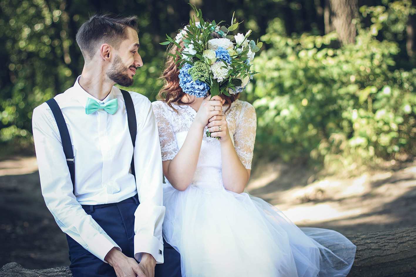Groom smiling at Bride hidden behind floral bouquet